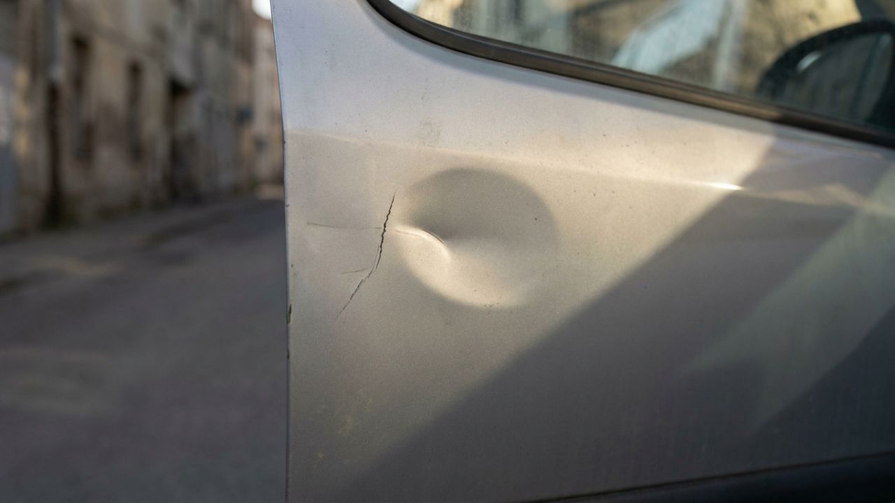 A small scratch and a shallow dent on a silver car door